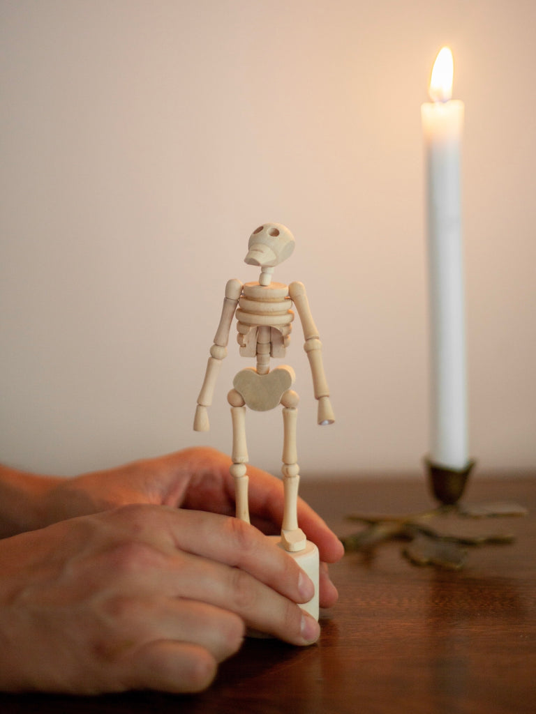 Someone holding a small wooden movable figure of a skeleton by a candle. 