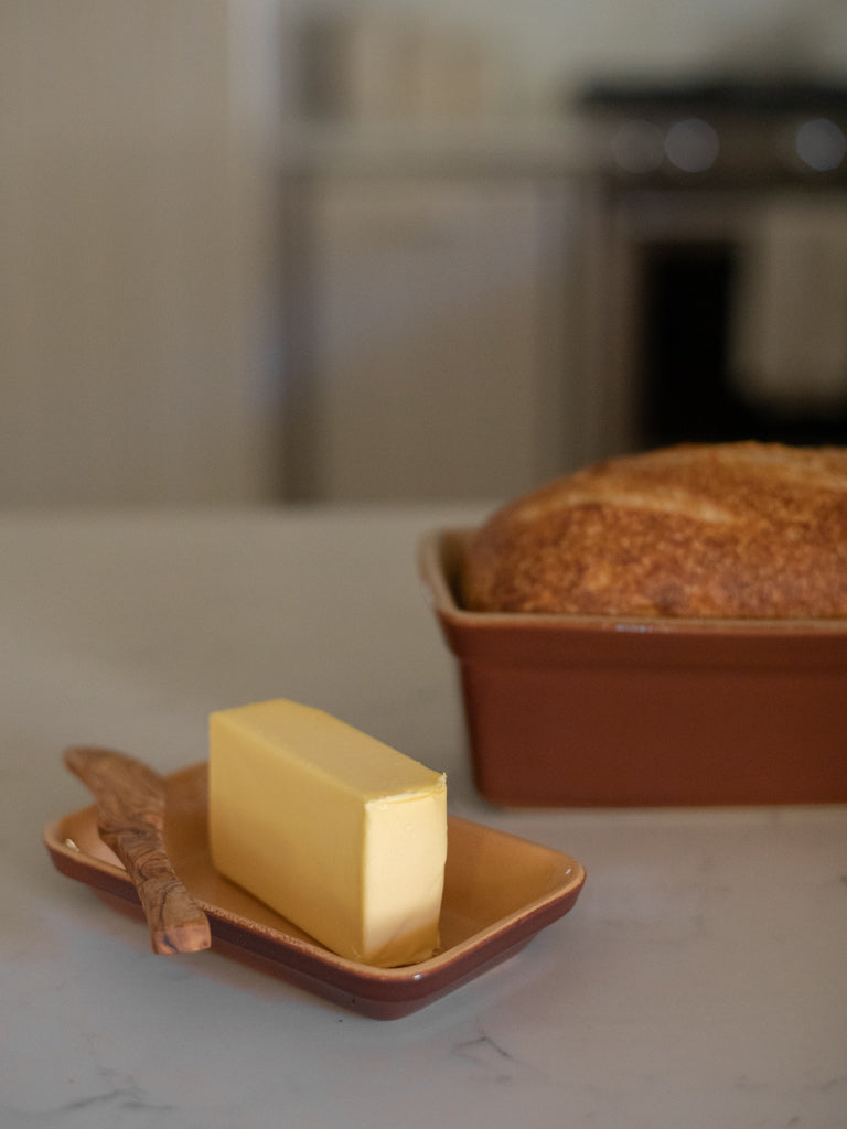 A dish of butter with a wooden knife next to a pan of bread. 