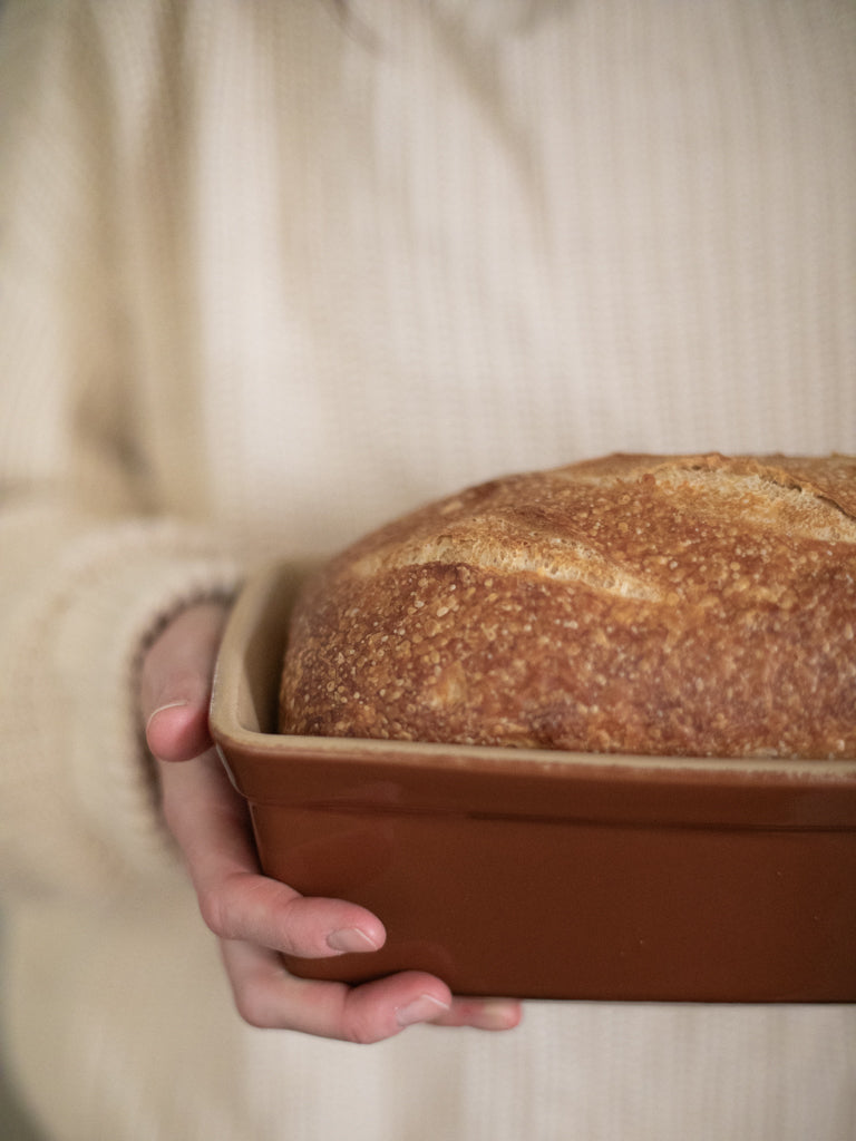 A person holding a loaf of bread in a loaf pan. 