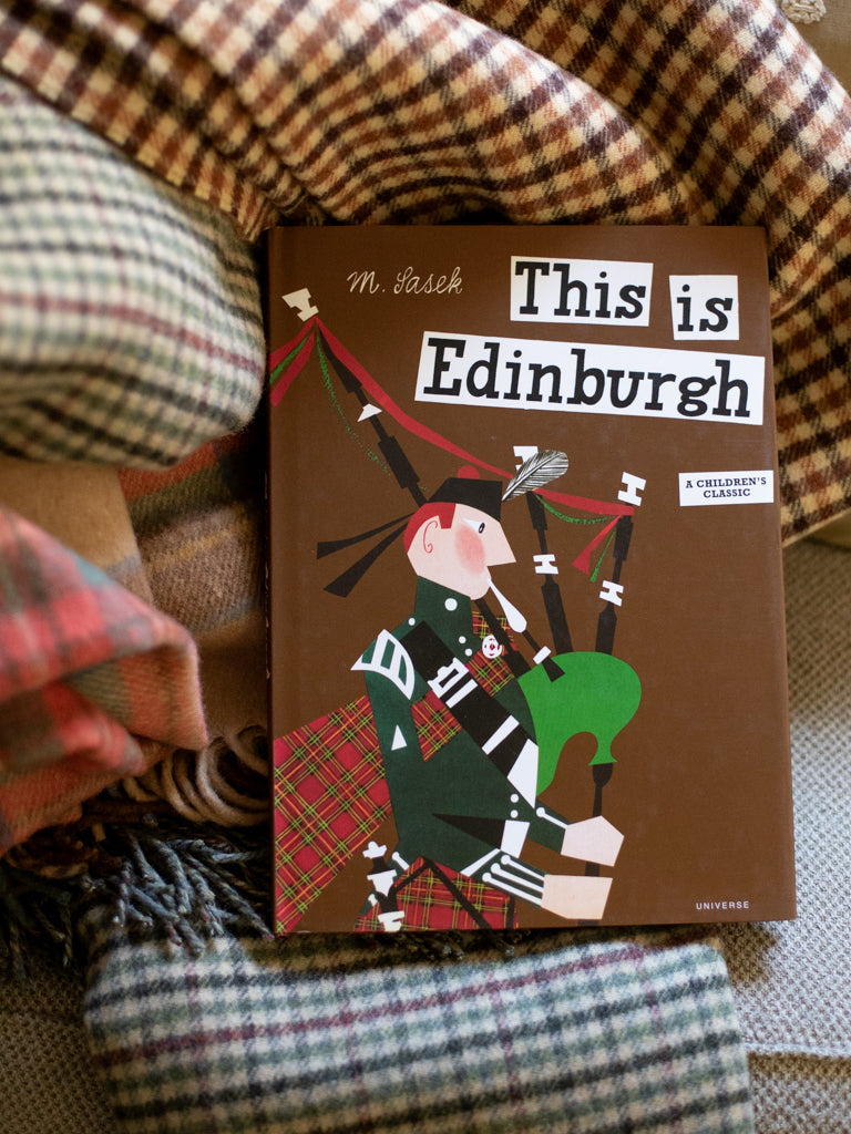 Brown family friendly book cover labeled "This is Edinburgh". Image on cover shows man playing bagpipes.