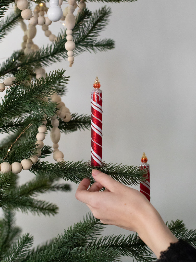 A red and white striped glass candle with a fake fire sitting upon the top as it is held next to a Christmas tree.