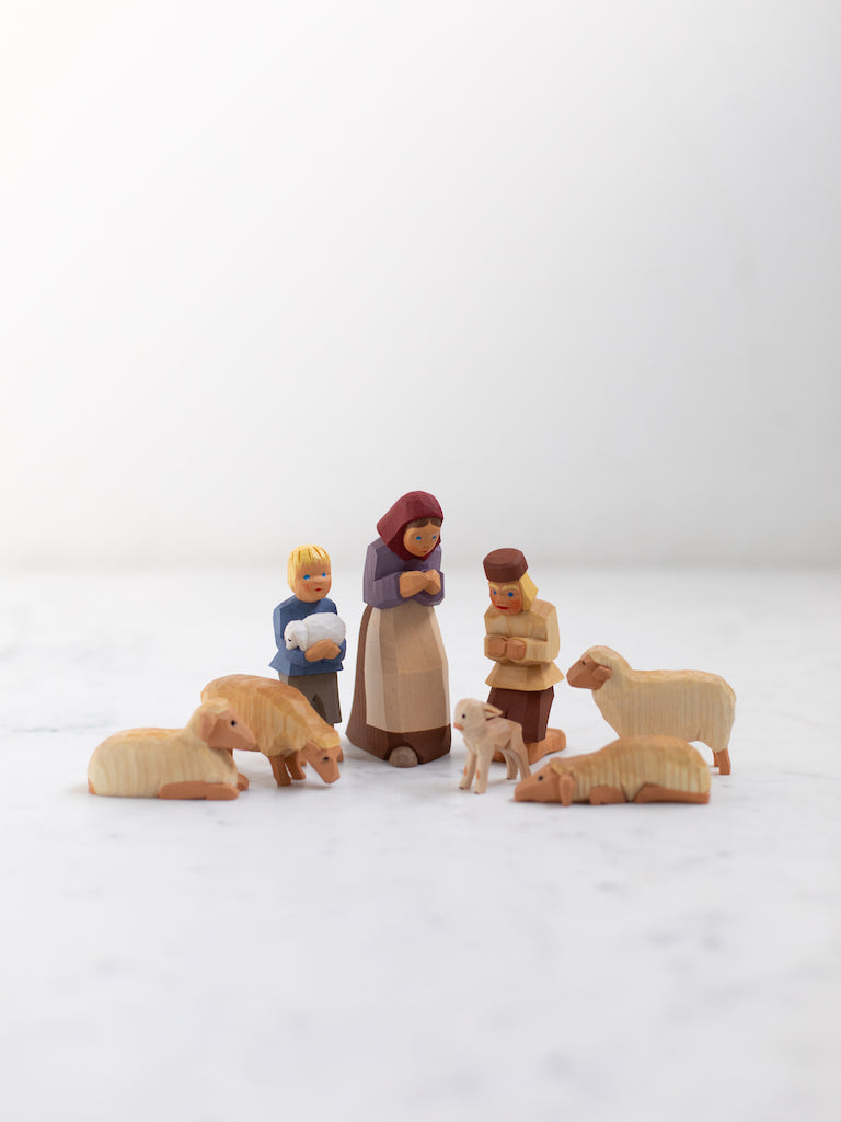 Wooden figures of a woman and two young boys, all bowing and kneeling, surrounded by four sheep in various positions.