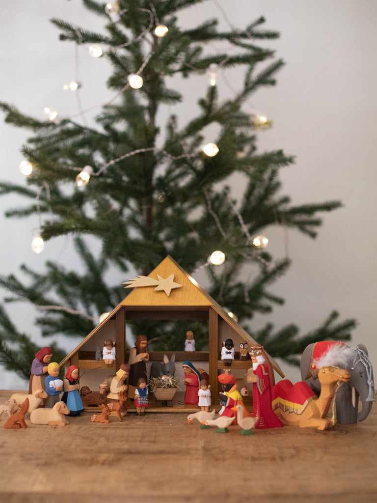 A nativity scene including all characters under a manger, with a Christmas tree in the far background.