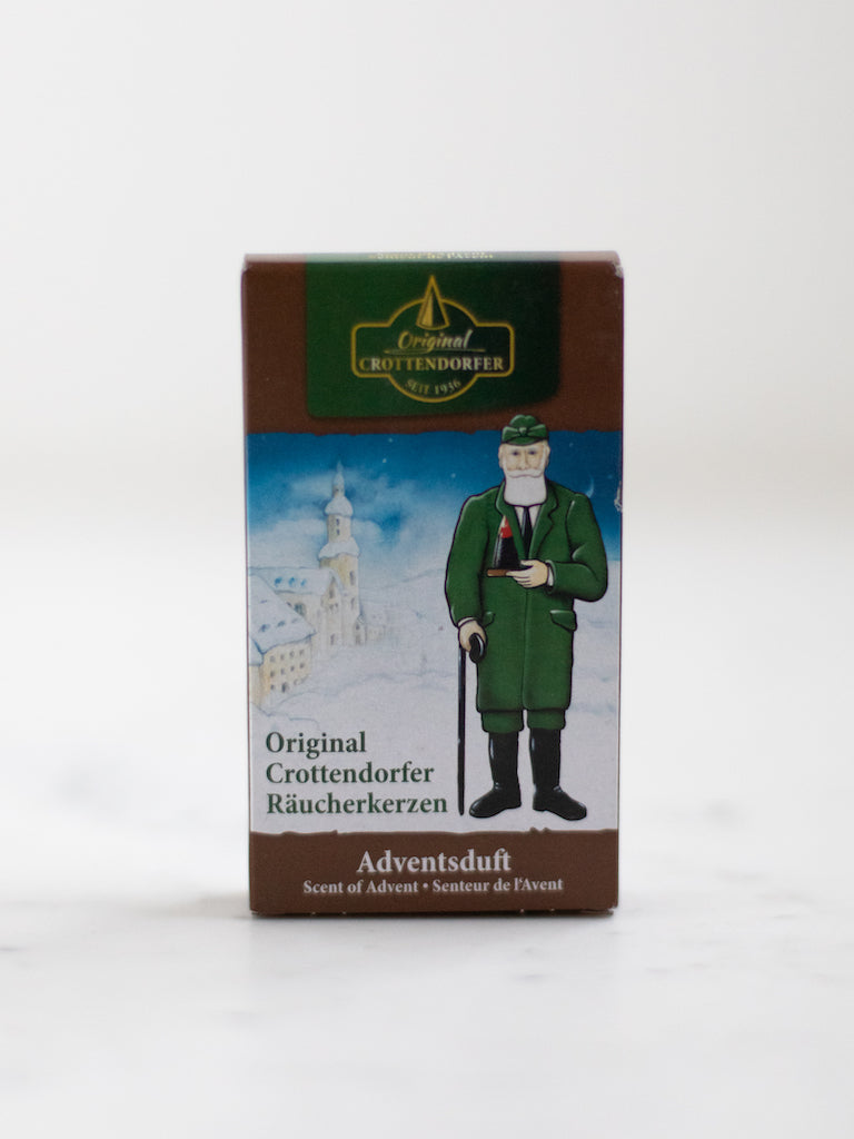 A box cover of an incense scent with an old man in a green coat and pants standing in the snow.