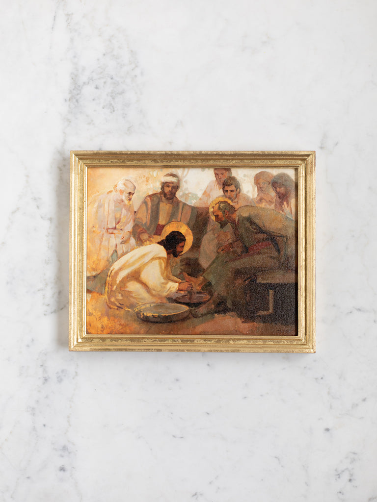 A painting print in a gold frame depicting Christ washing his disciple’s feet.