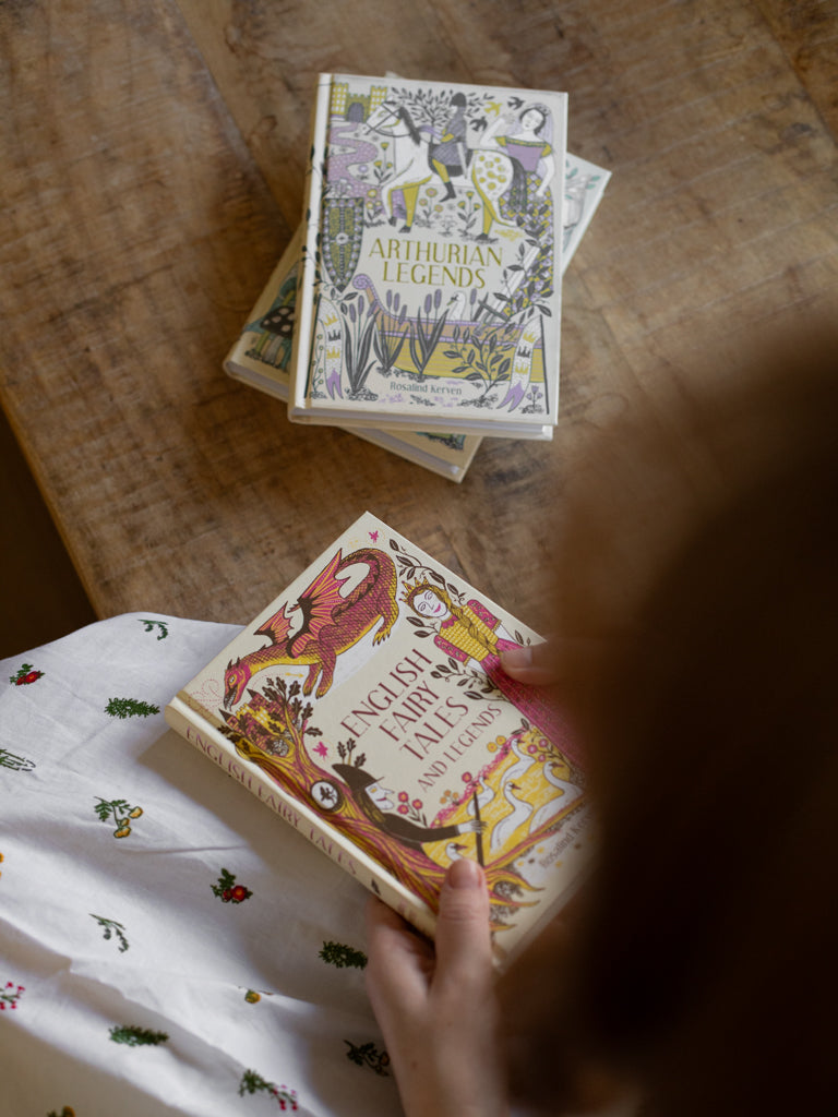 Person sitting with English Fairy Tales in their lap beside a copy of Arthurian Legends and Faeries Elves and Goblins. 