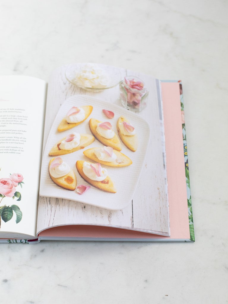 A cookbook opened to a photo of a dessert with rose petals. 