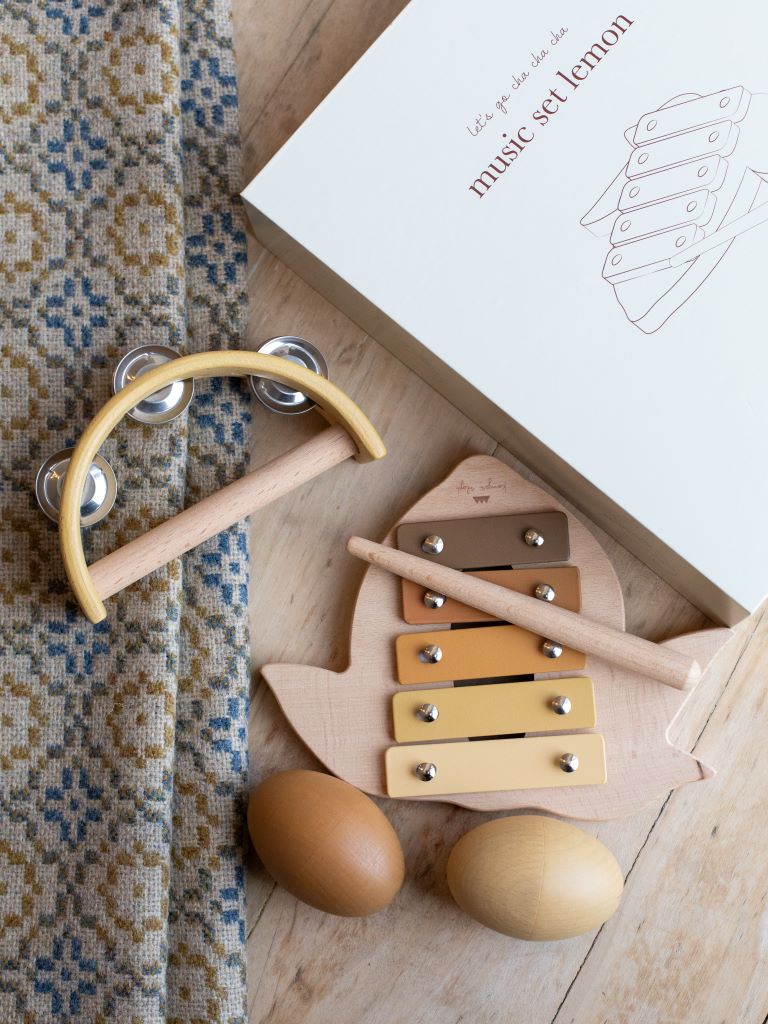 A tambourine, a lemon shaped xylophone, and two egg shaped maracas by a box with a picture of the lemon shaped xylophone on it under a blanket.   
