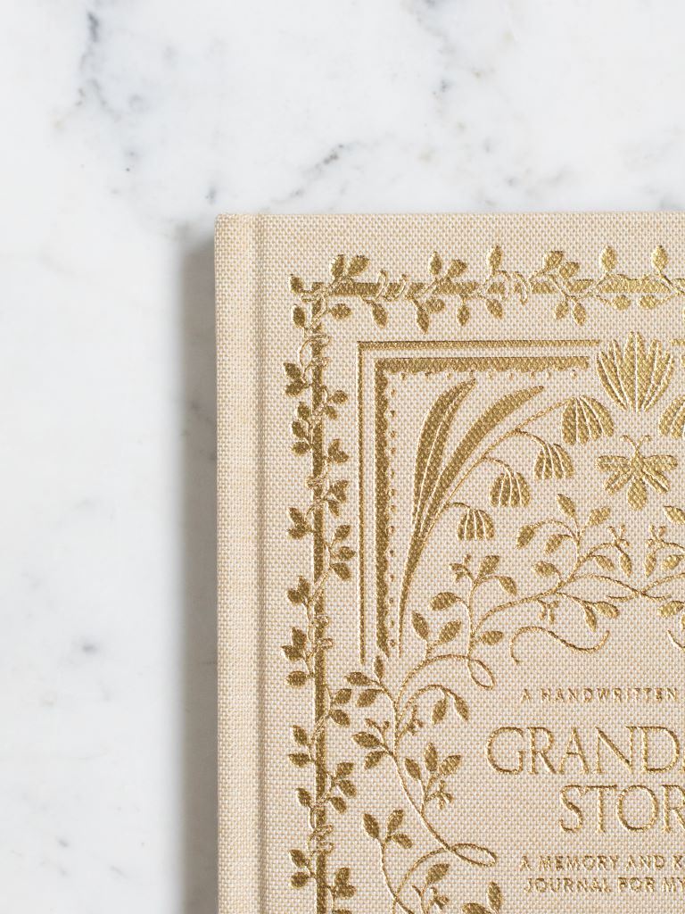 A close up photo of the gold designs of flowers on a cream clothbound book. 