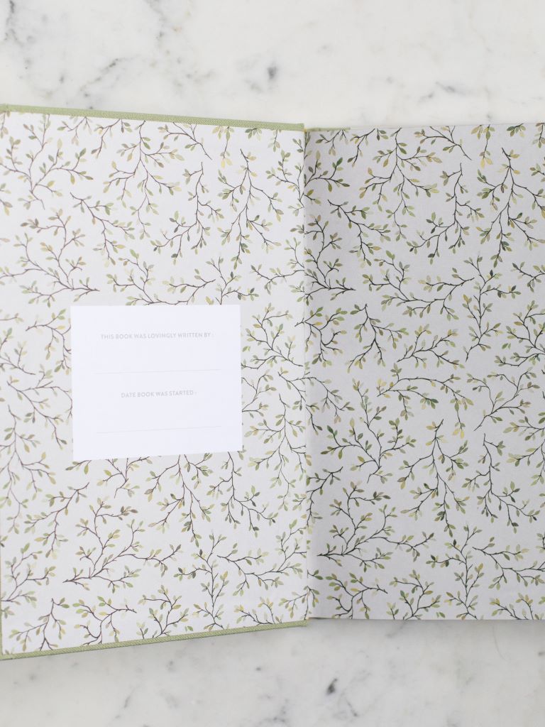 A book opened up to a page covered in a vine design with a place to put the  name of the author and the date it was started.