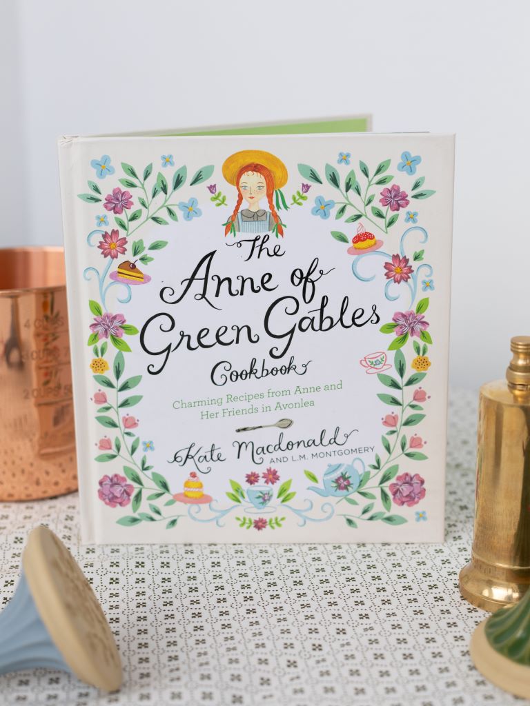 Front view of Anne of Green Gables cookbook with floral detailing and an illustration of a red-headed girl with an orange straw hat.