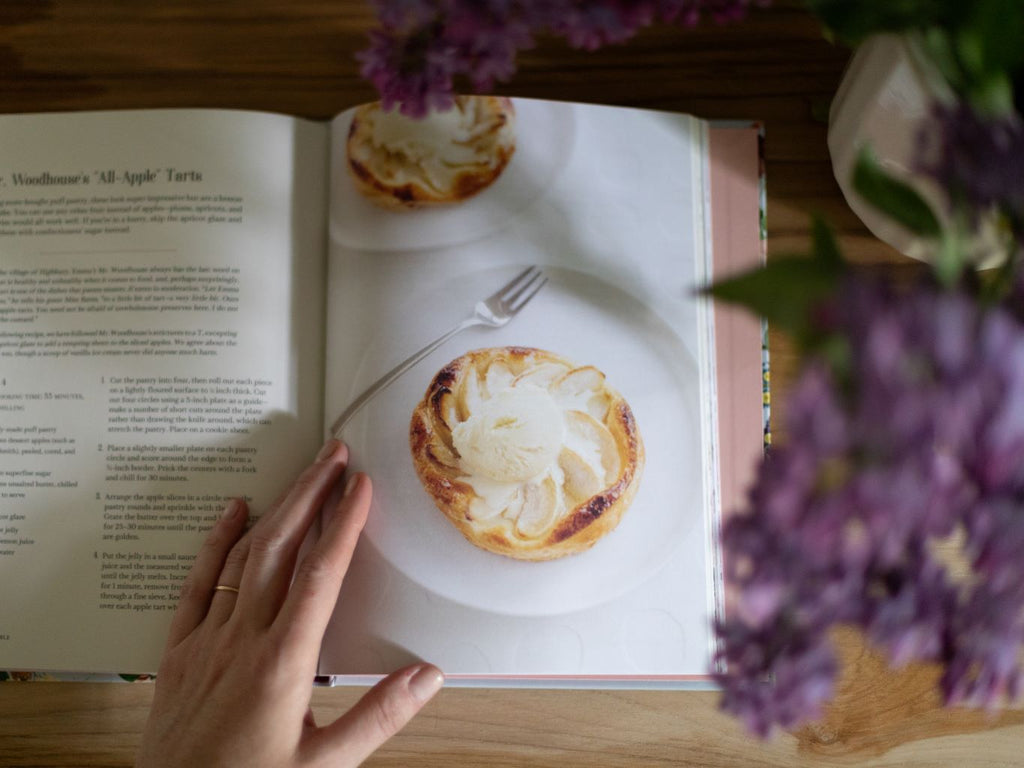 A person opening a cookbook to a recipe for an apple tart. 