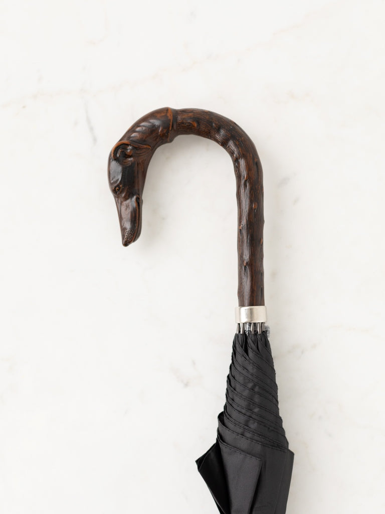 A dark wood curved umbrella handle, with the end shaped into the face and neck of a dog.