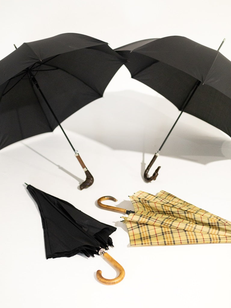 Two black open umbrellas sitting on the floor, with a black and yellow checkered umbrella closed, as well as a black umbrella closed, both laying under the open ones.