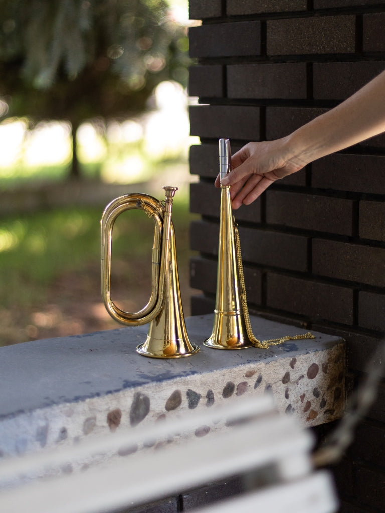 A brass trumpet and bugle sitting on a stone and cement bench outside.