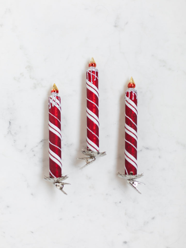 A red and white striped glass candle with a fake fire sitting upon the top with silver clips on the bottom.