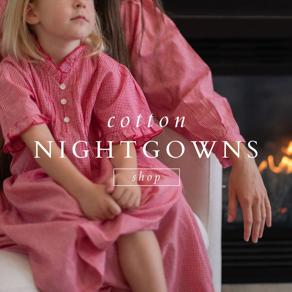 Two girls in red gingham nightgowns by the fireplace.
