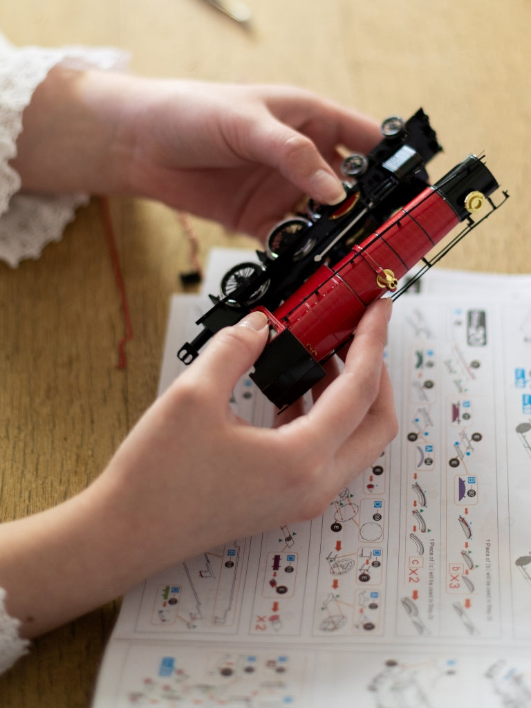 Two hands holding the red train model.