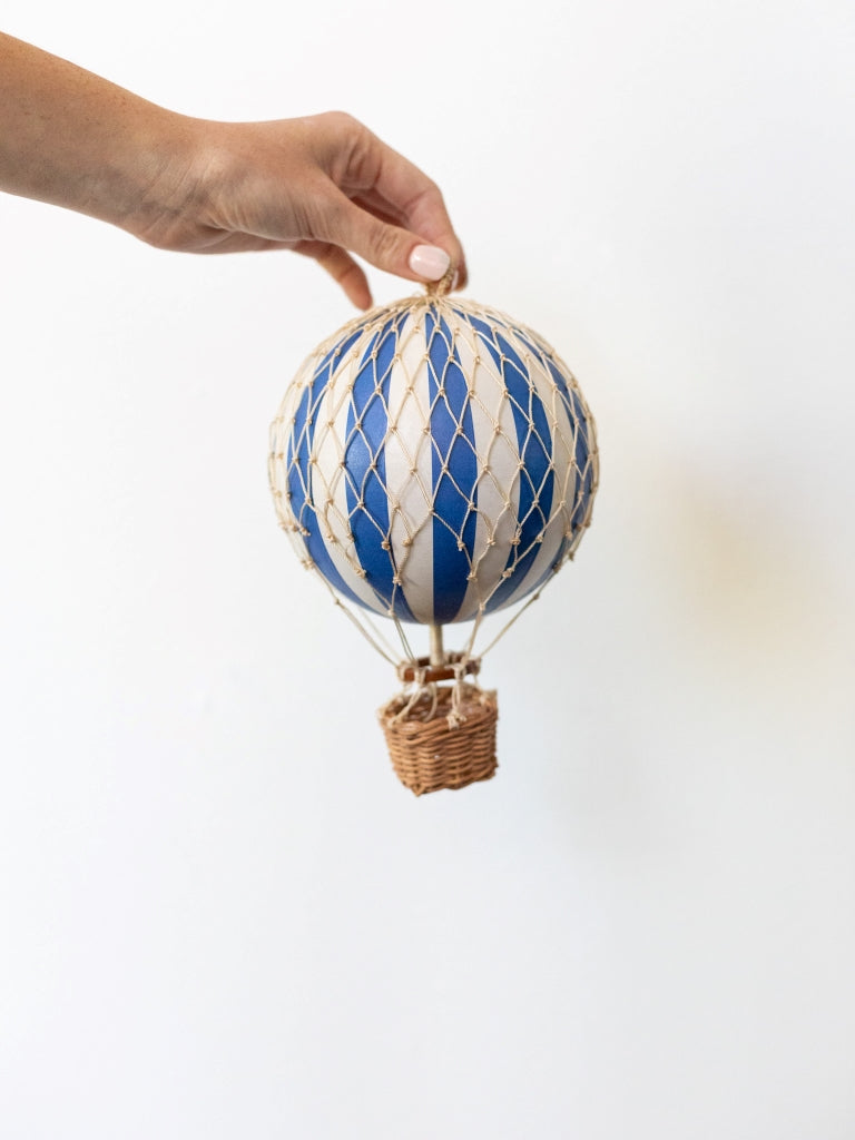 Medium blue and white striped balloon, covered in net with a small, woven basket connected to the bottom.