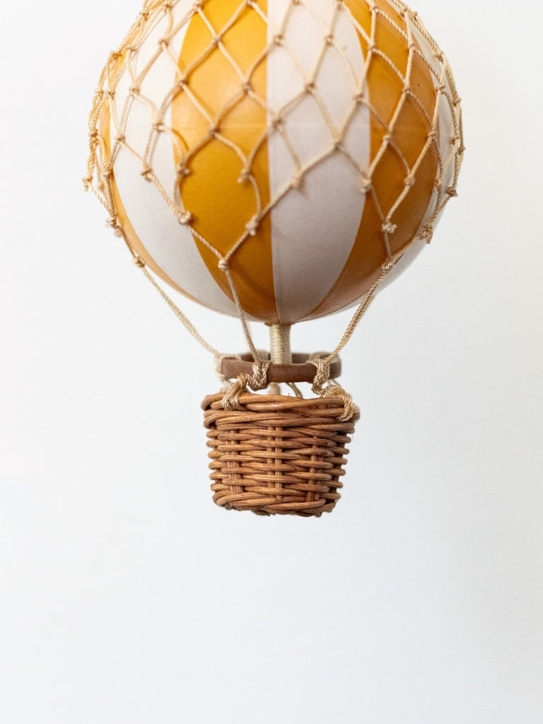 Small yellow and white striped balloon, covered in net with a small, woven basket connected to the bottom.