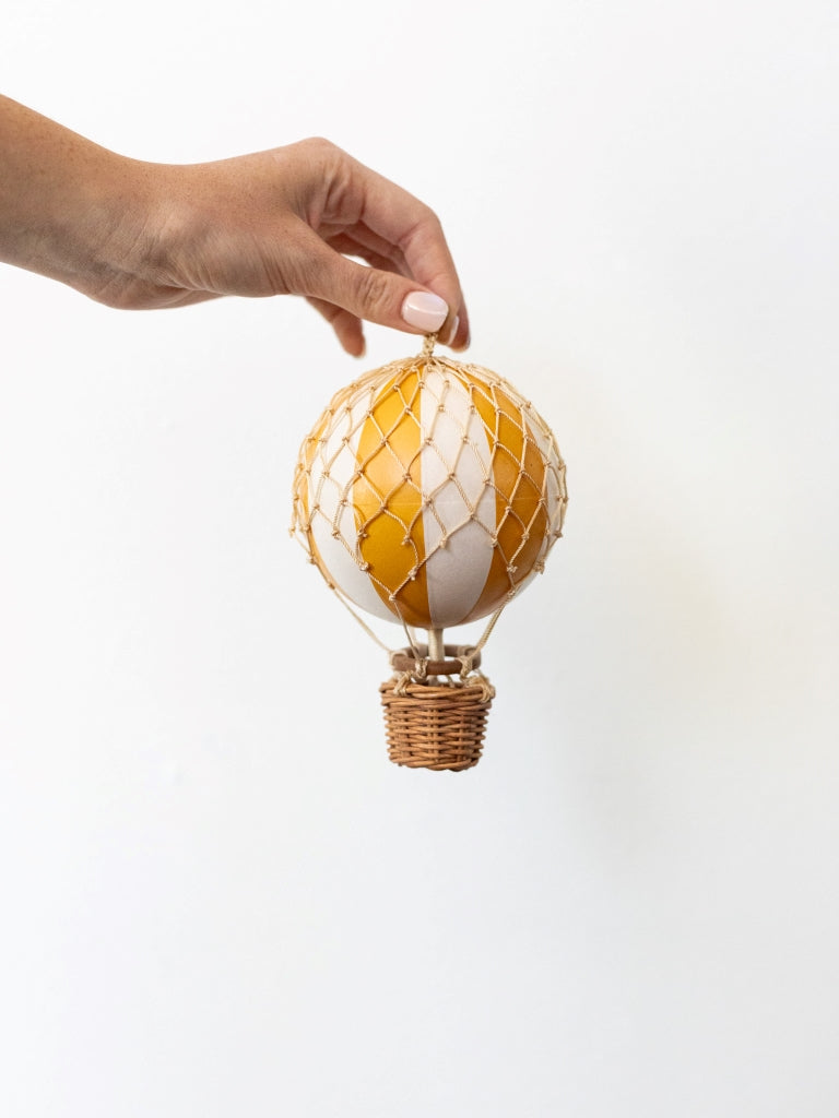 Yellow and white striped ballon, covered in net with a small, woven basket connected to the bottom.