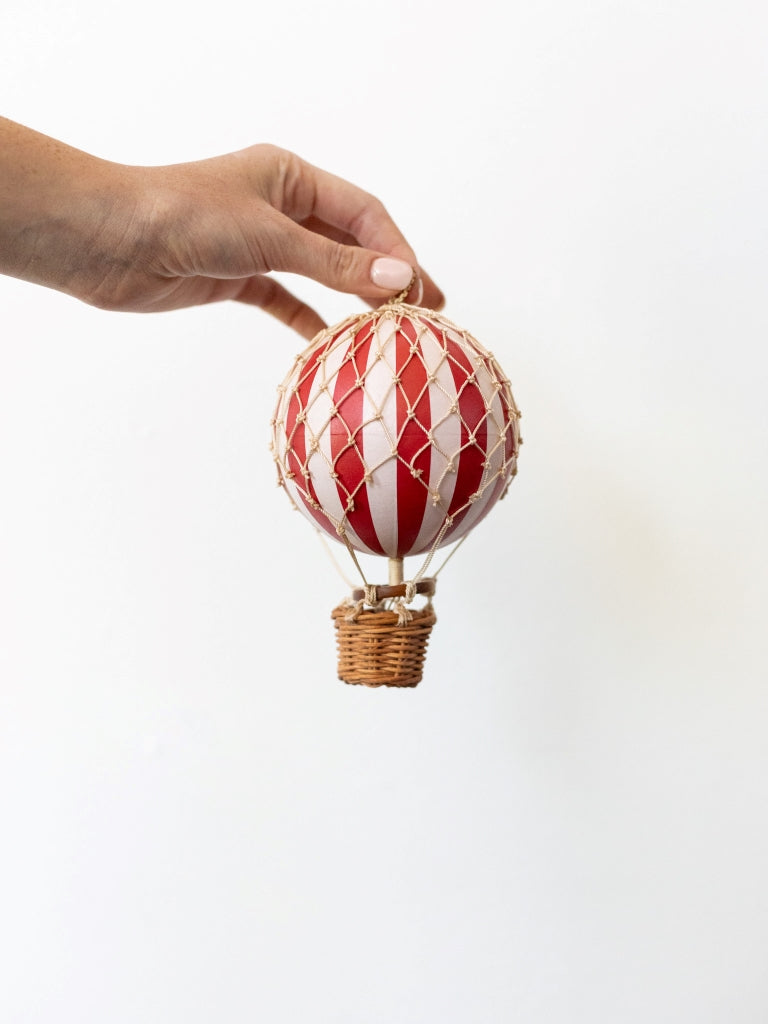 Small red and white striped balloon, covered in net with a small, woven basket connected to the bottom.