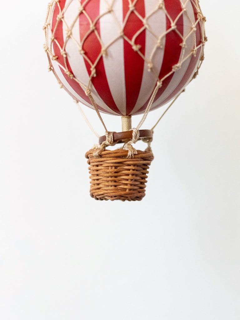 A small red and white striped ballon, covered in net with a small, woven basket connected to the bottom.