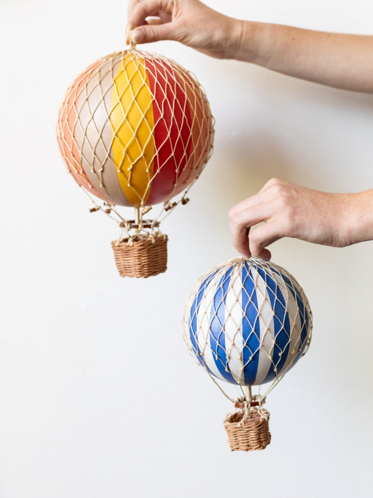 A medium blue and white striped held next to a large multicolor striped hot air balloons, covering in net with small, woven baskets connected to their bottom.