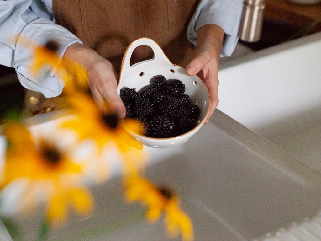 Woman stands over sink with colander filled with berries.