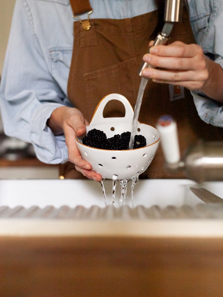 Woman washes berries in colander over a sink.