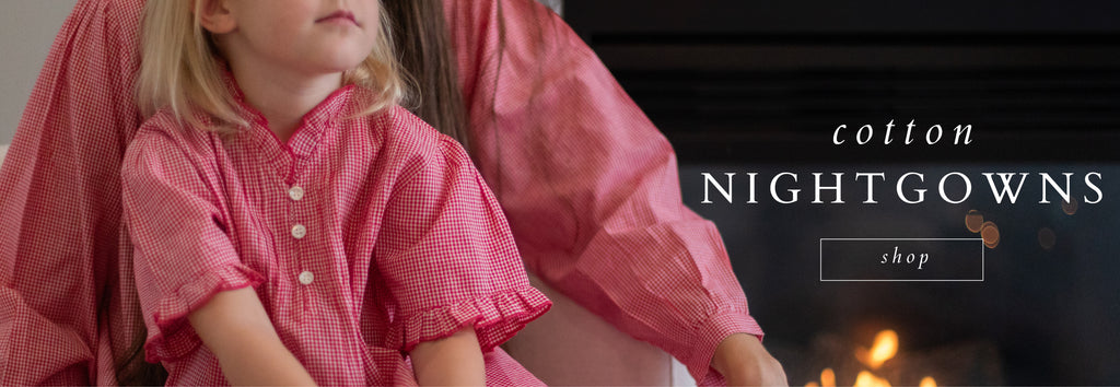 Two girls in red gingham nightgowns by the fireplace.