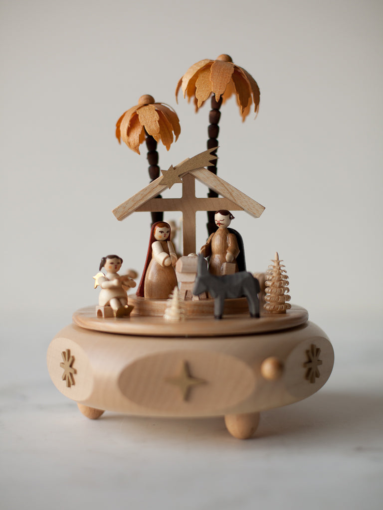 Circular wooden music box with a figurine nativity. Includes Mary, Joseph, baby Jesus, an angel, and a donkey.