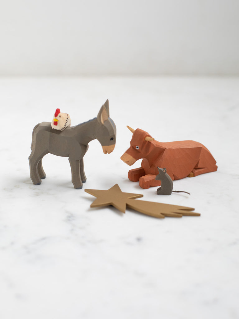 Wooden figurines of four animals, a donkey, cow, chicken, and rat, with a wooden depiction of a shooting star laid in front of them.