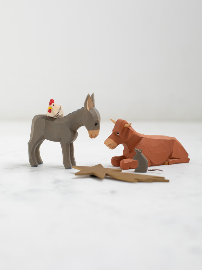 Wooden figurines of four animals, a donkey, cow, chicken, and rat, with a wooden depiction of a shooting star laid in front of them.
