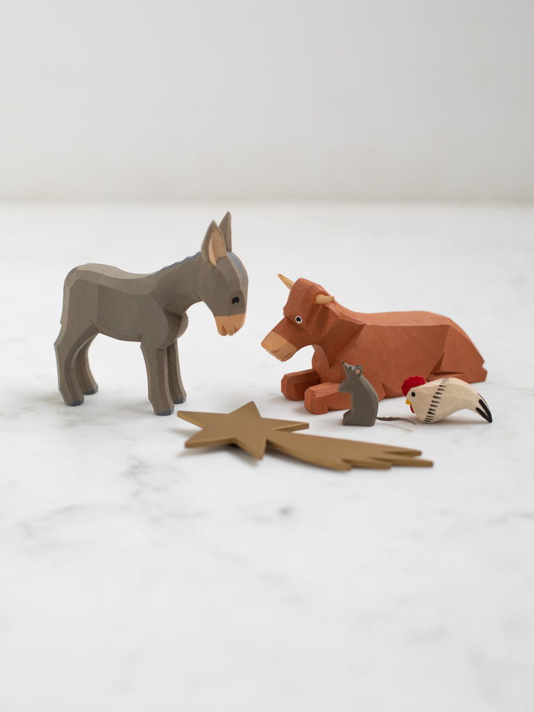Wooden figurines of four animals, a donkey, cow, chicken, and rat, with a wooden depiction of a shooting star laid in front of them.