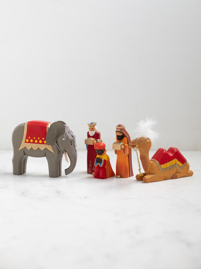 The three kings holding their gifts, all bowing and one kneeling. A wooden elephant figurine and a sitting camel figurine.