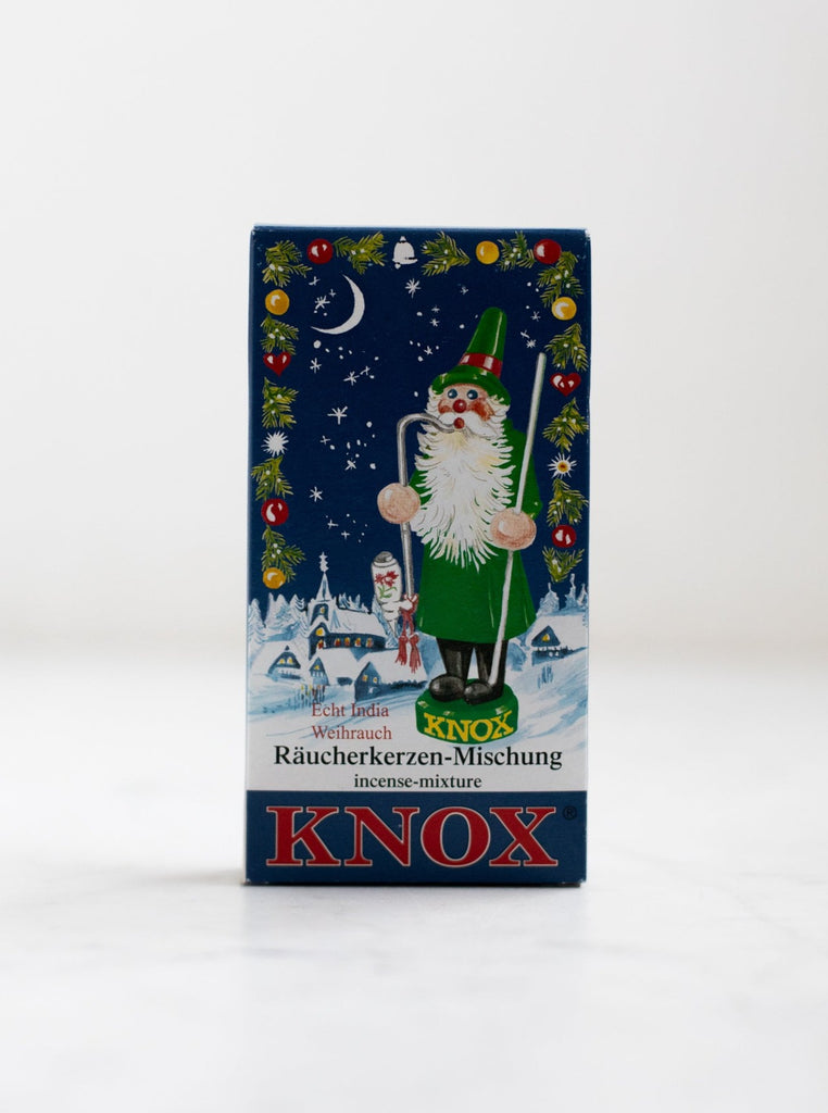 A box cover of an incense scent with a Christmas style character and a snowy village with Christmas decorations.