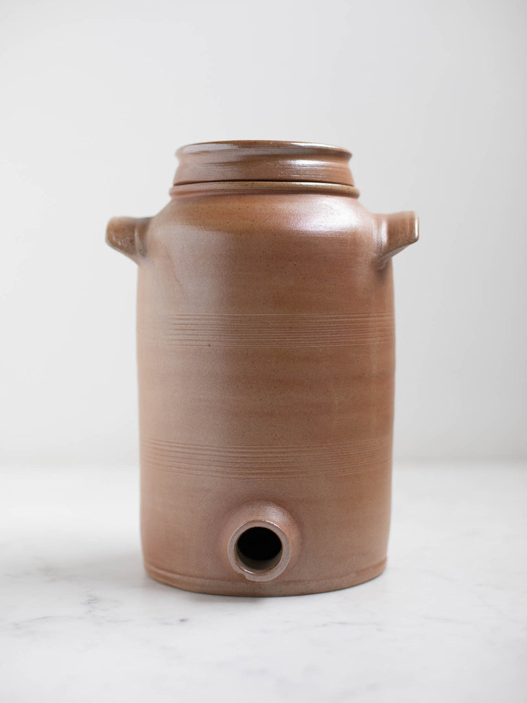 A tall light brown water jug without its spout. 