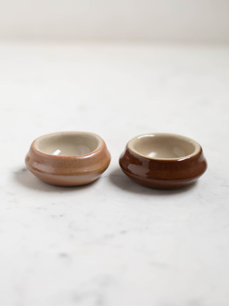 Two small wide circle dishes, one light brown, one dark. 