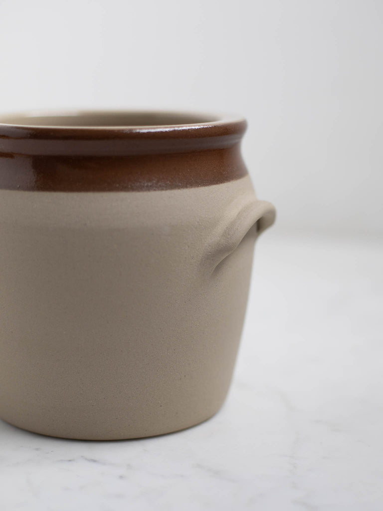 The side of a white barrel crock with a brown rim and built in handles. 