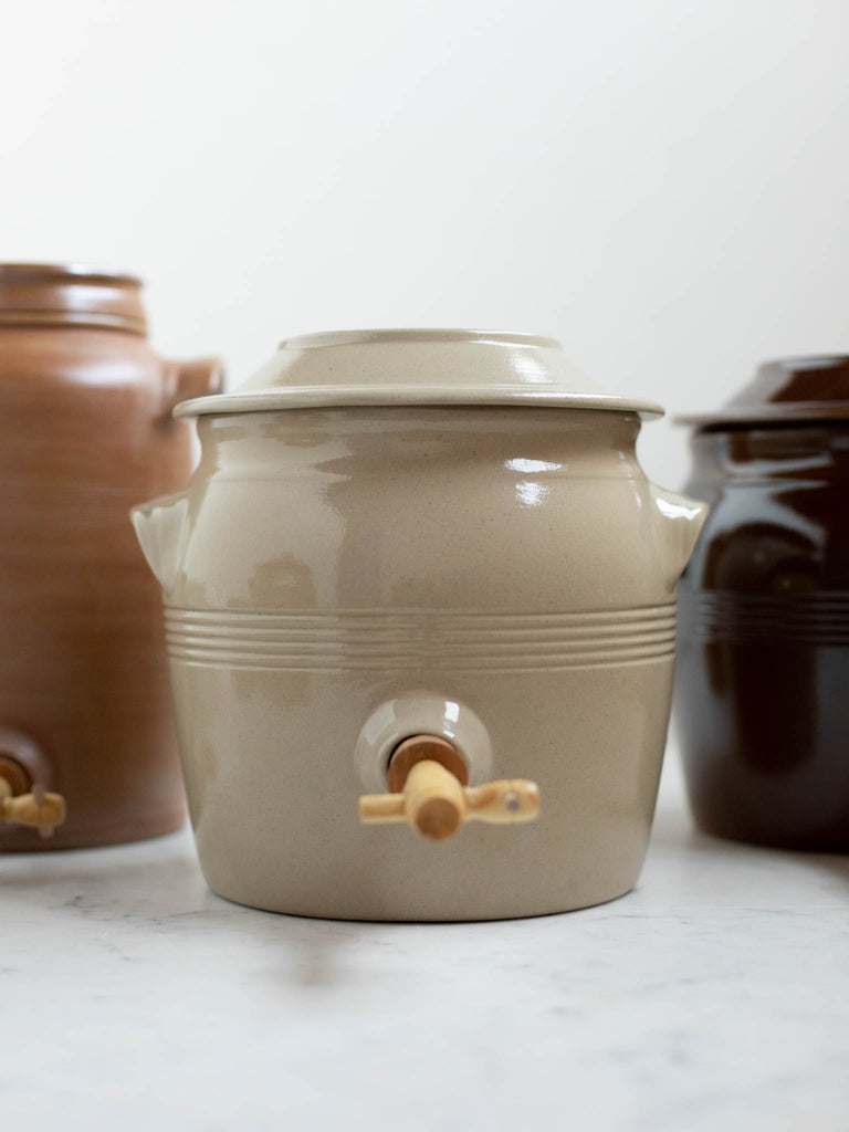 Short white water jug next to a black water jug and a brown water jug. 