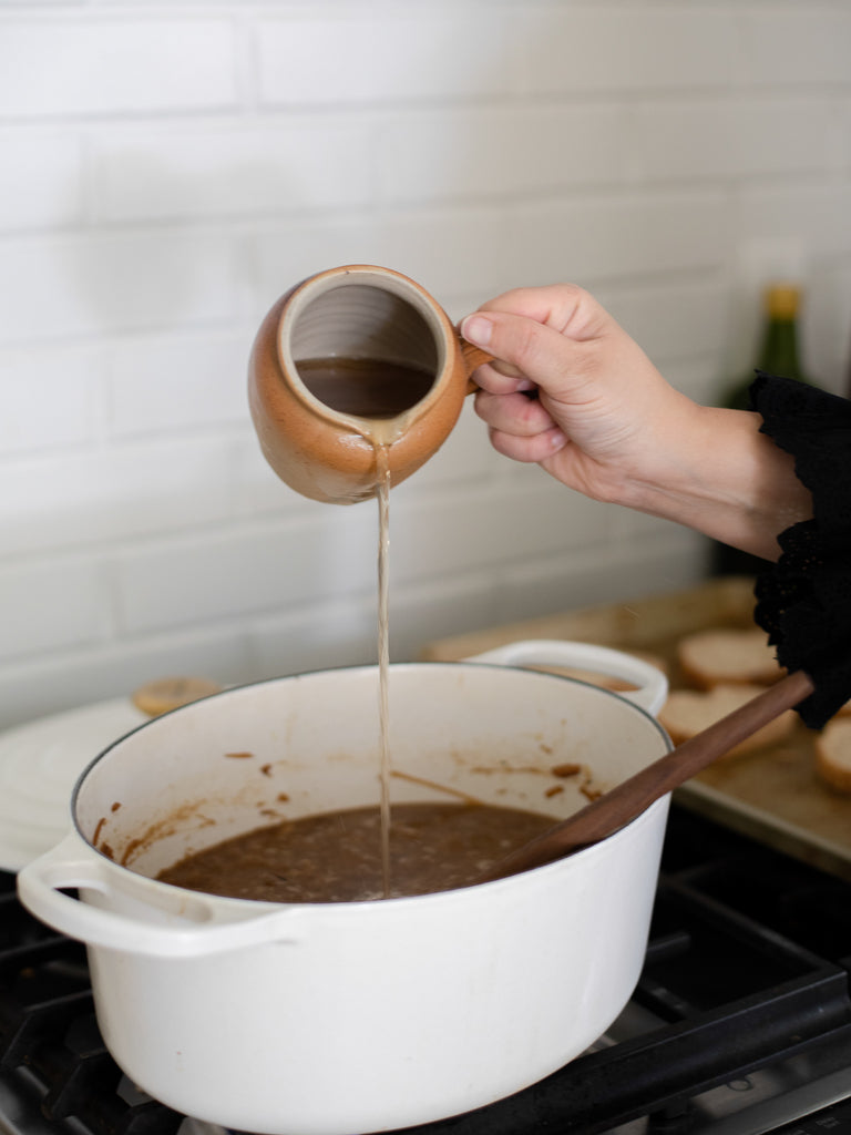 Someone using a sauce pot to pour a liquid into a soup pot. 