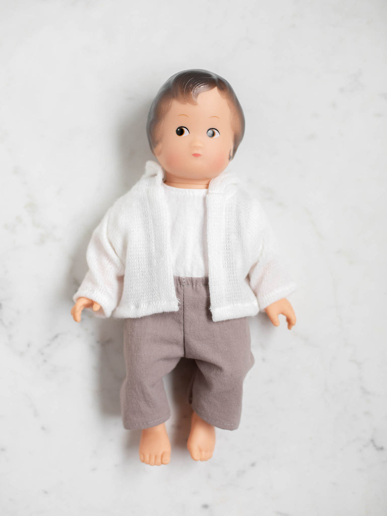Baby doll with muted plum pants, a white shirt, and a white cotton sweater. This baby doll has dark brown hair and a light skin tone.