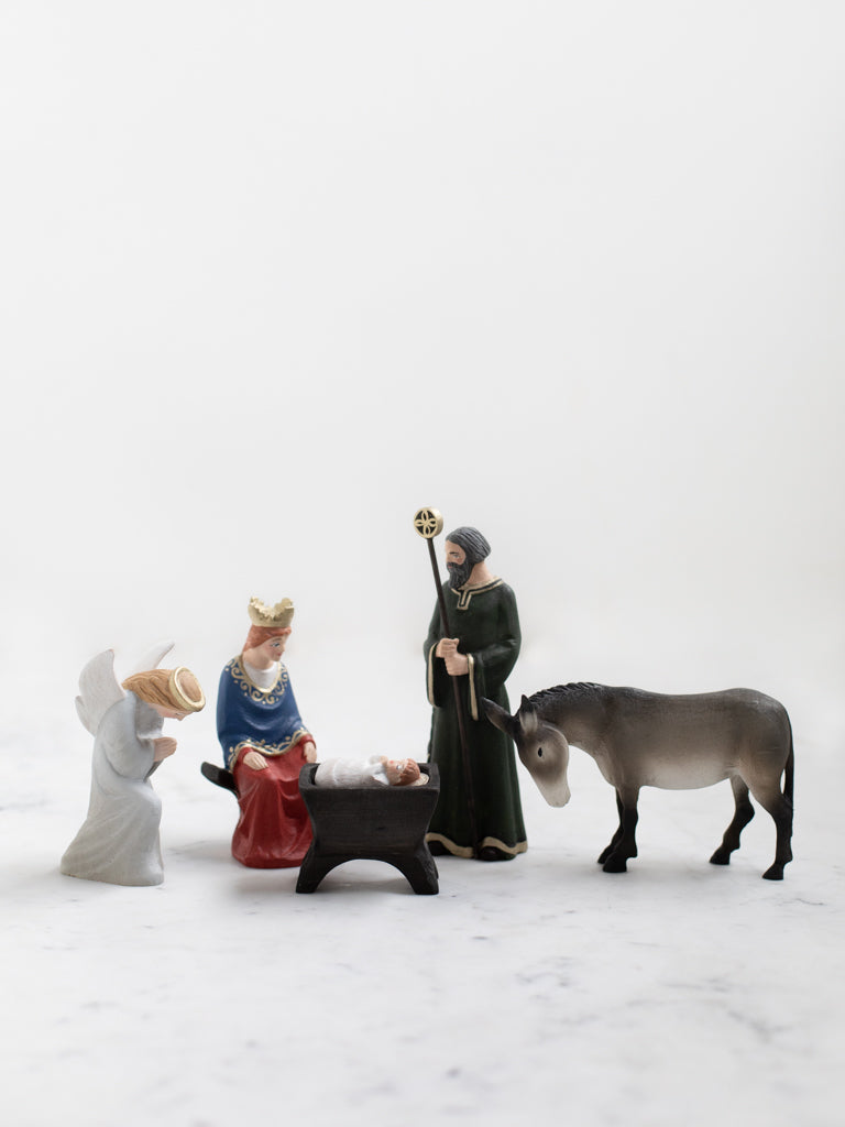 Mary, Joseph, and baby Jesus figurines accompanied by a kneeling angel and bowing donkey.