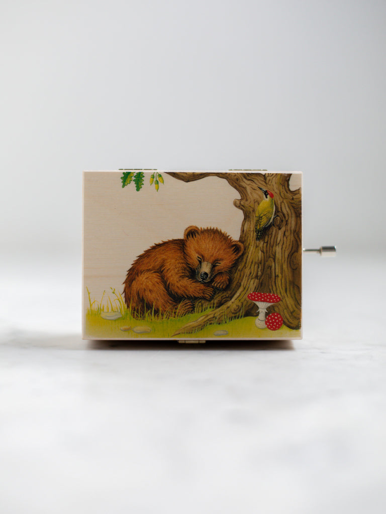 An alpine music box with a sleeping bear up against a tree trunk with a mushroom nearby.