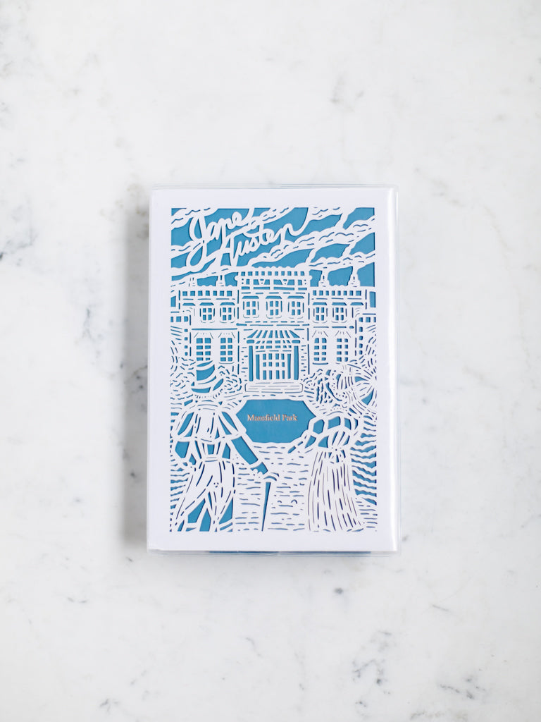 A blue book with a white paper cut design over it of a man in a hat and a woman in a bonnet looking at a large mansion house. 