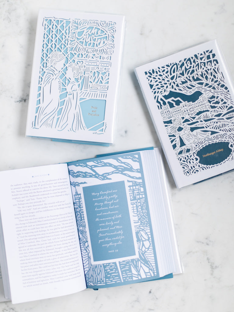 Three books with paper cut designs on them, one opened to a quote on a page. 