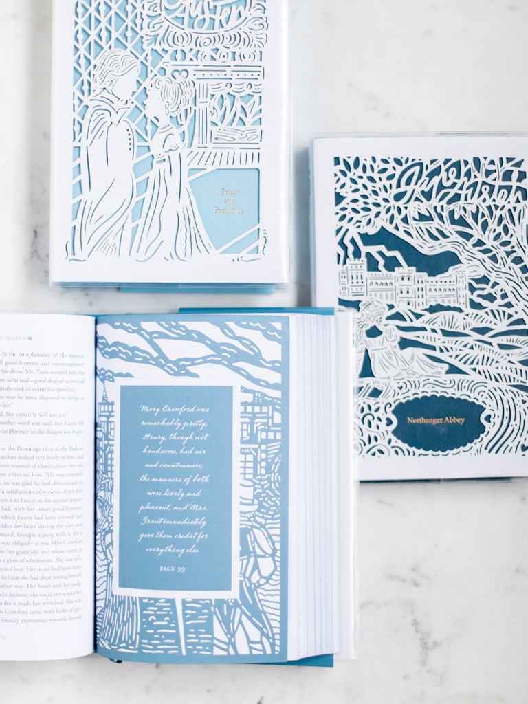 Three books with paper cut designs on them, one opened to a quote on a page. 