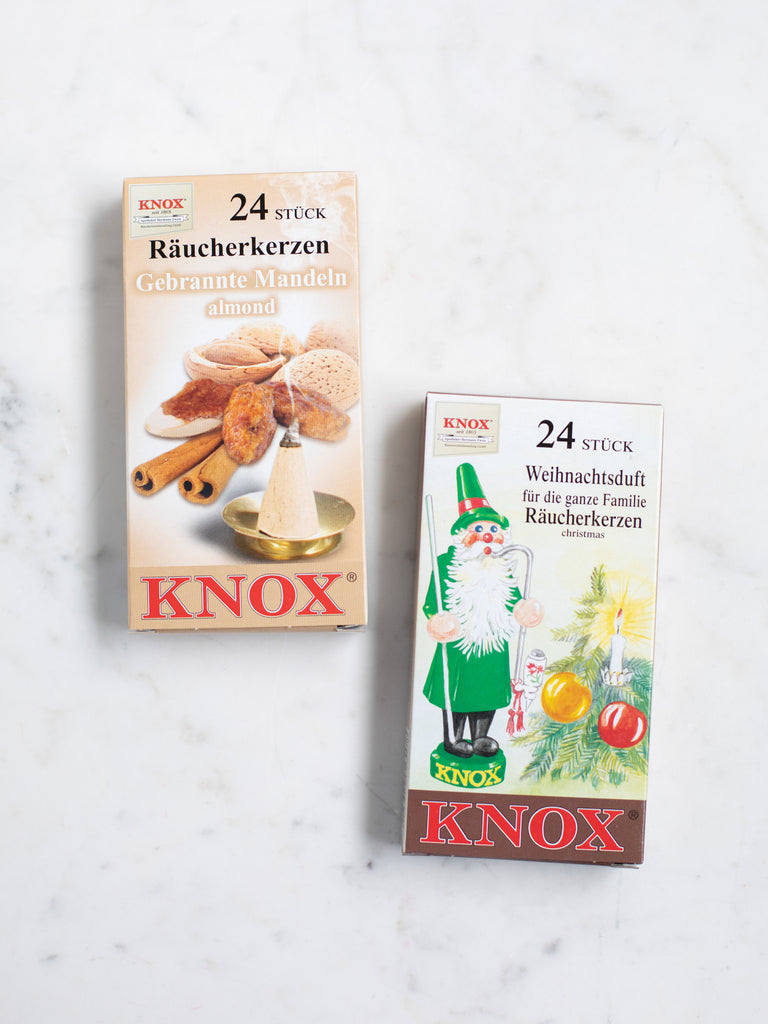 Two front covers of small incense cone boxes, one green with a Christmas tree and figure, and one with photos of nuts and cinnamon.