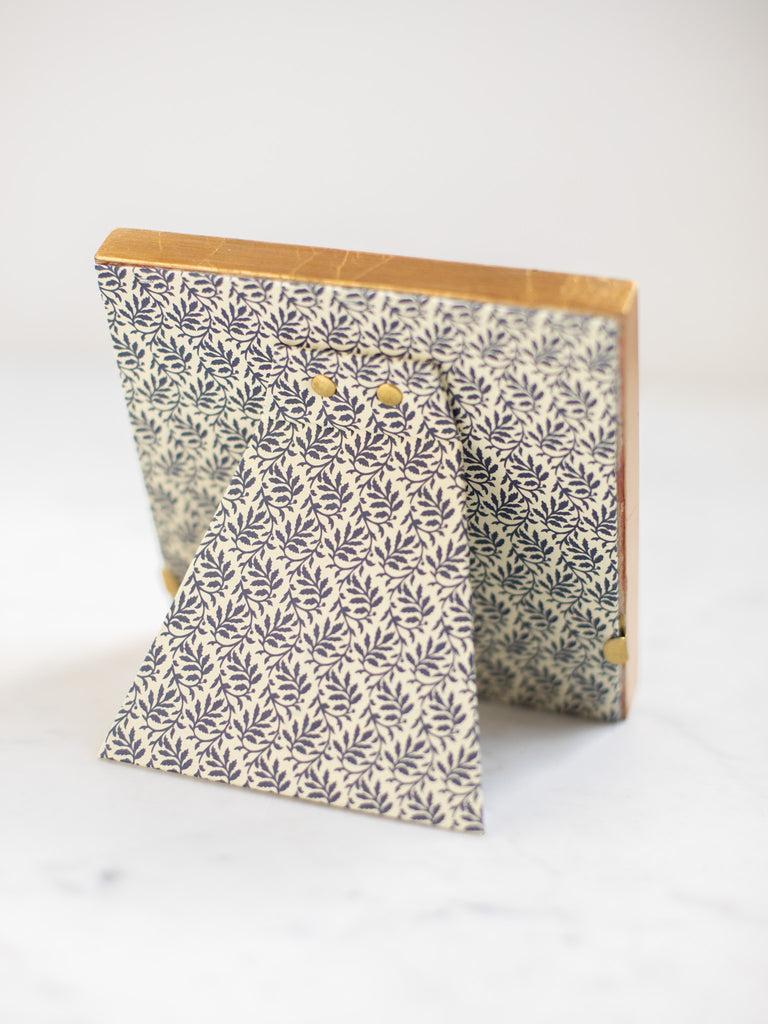 The back of the gold frames, a dark blue leaf batter covering the back of the frame and its stand.